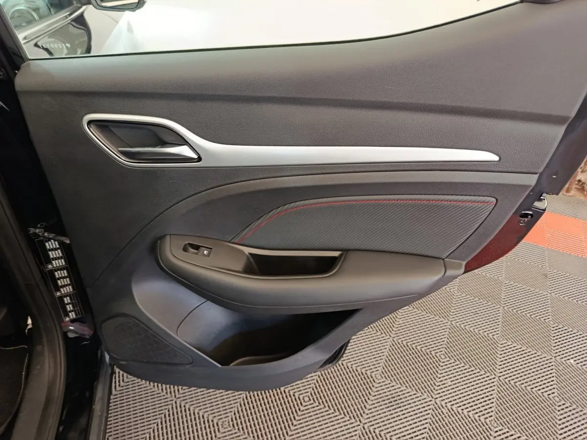 Vue intérieure du panneau de porte avant gauche noir avec surpiqûres rouges du MG ZS Luxury 2024 électrique.