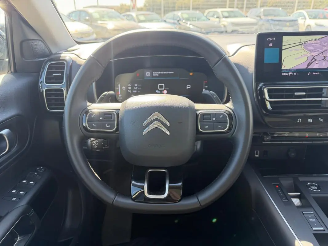 Vue intérieure centrée sur le volant noir du Citroën C5 Aircross 2024 hybride avec tableau de bord numérique et écran tactile.