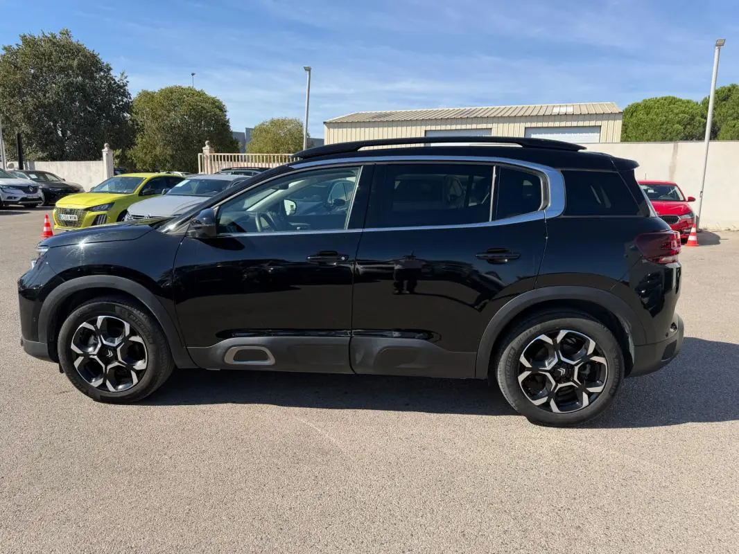 Vue de profil côté gauche d'un Citroën C5 Aircross hybride noir 2024 avec jantes distinctives et barres de toit.