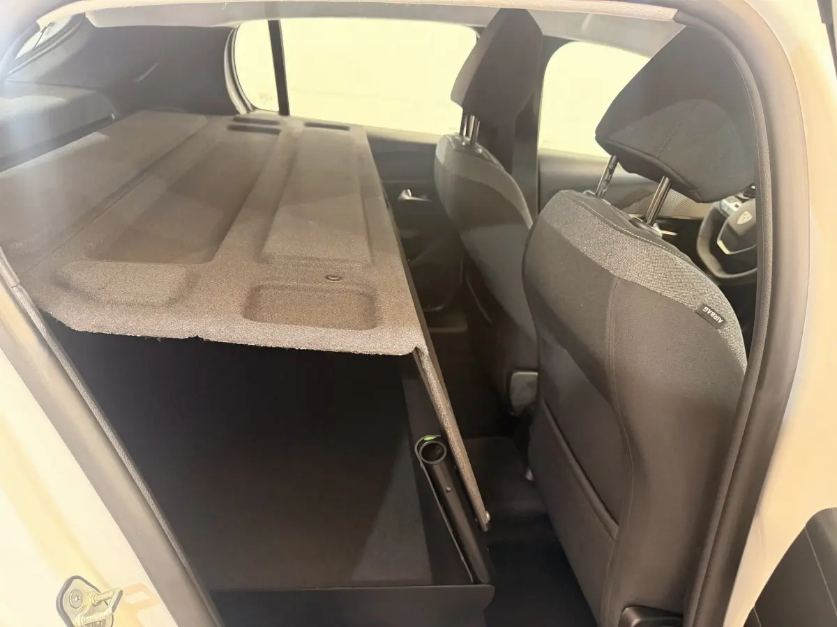 Vue intérieure côté droit de la Peugeot 208 blanche 2025, montrant les sièges avant et la banquette arrière rabattue.