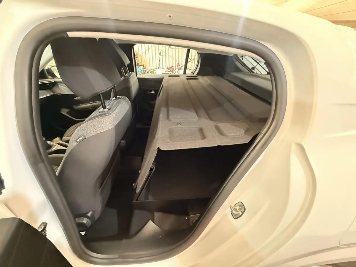 Vue intérieure côté droit de la Peugeot 208 blanche, montrant la banquette arrière avec cache-bagages relevé.