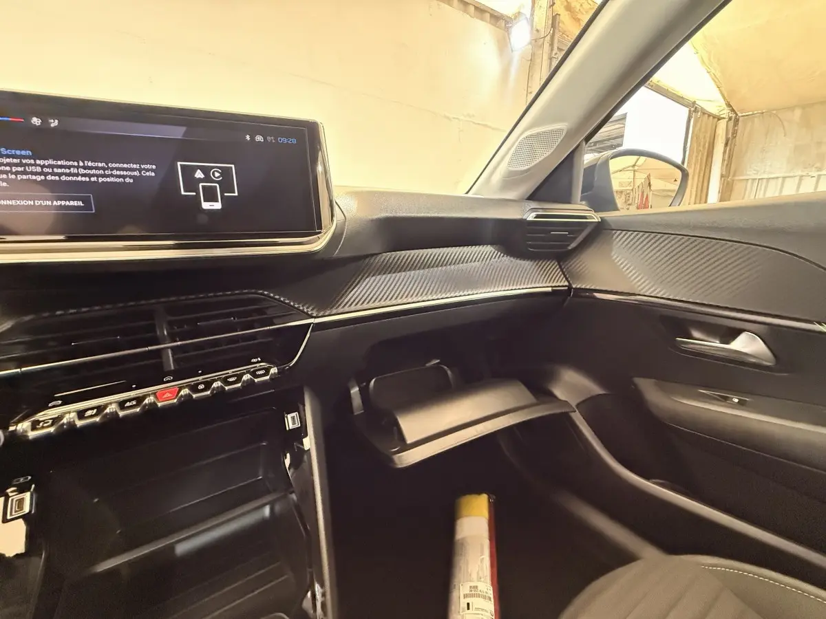 Vue intérieure côté passager de la Peugeot 208 blanche 2025, montrant tableau de bord et écran tactile central.