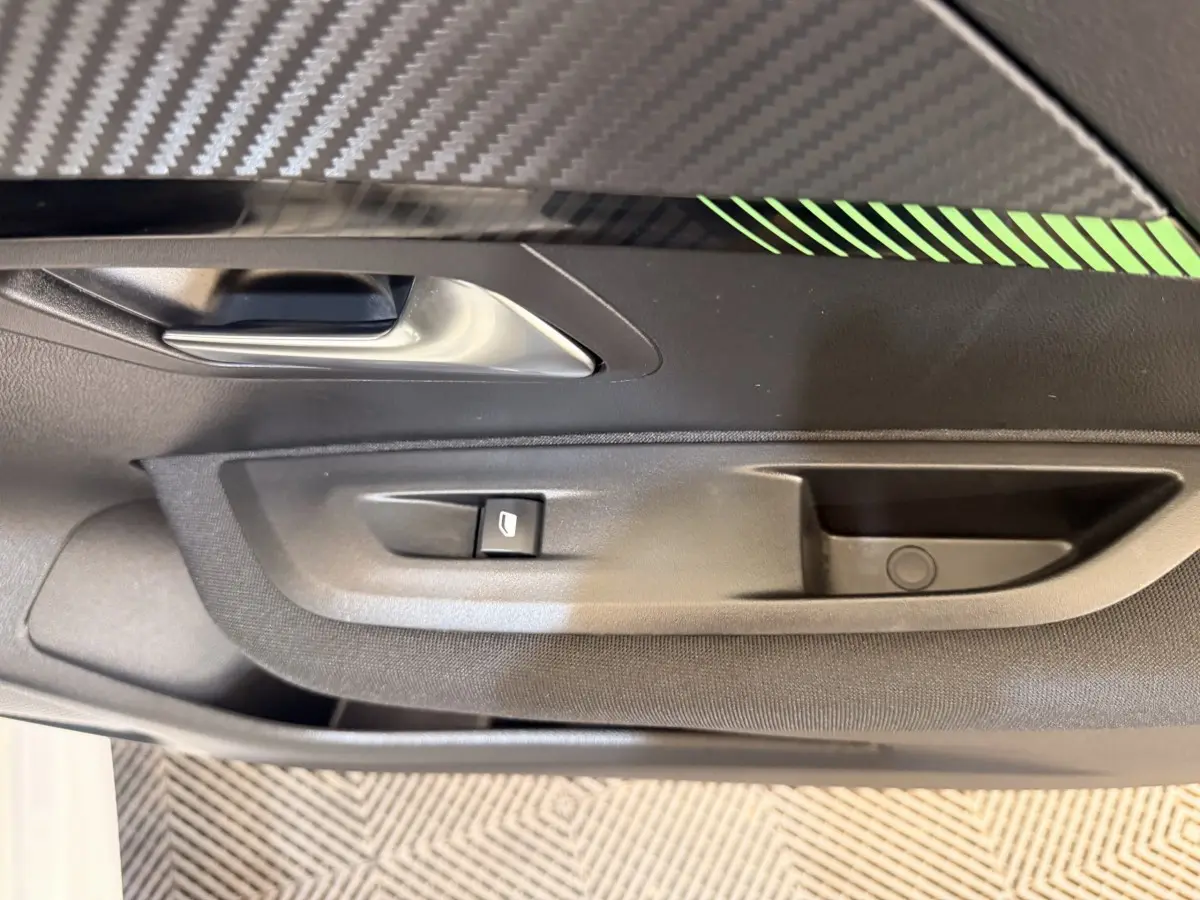 Gros plan sur la poignée intérieure et le bouton de lève-vitre côté gauche d’une Peugeot 208 blanche.