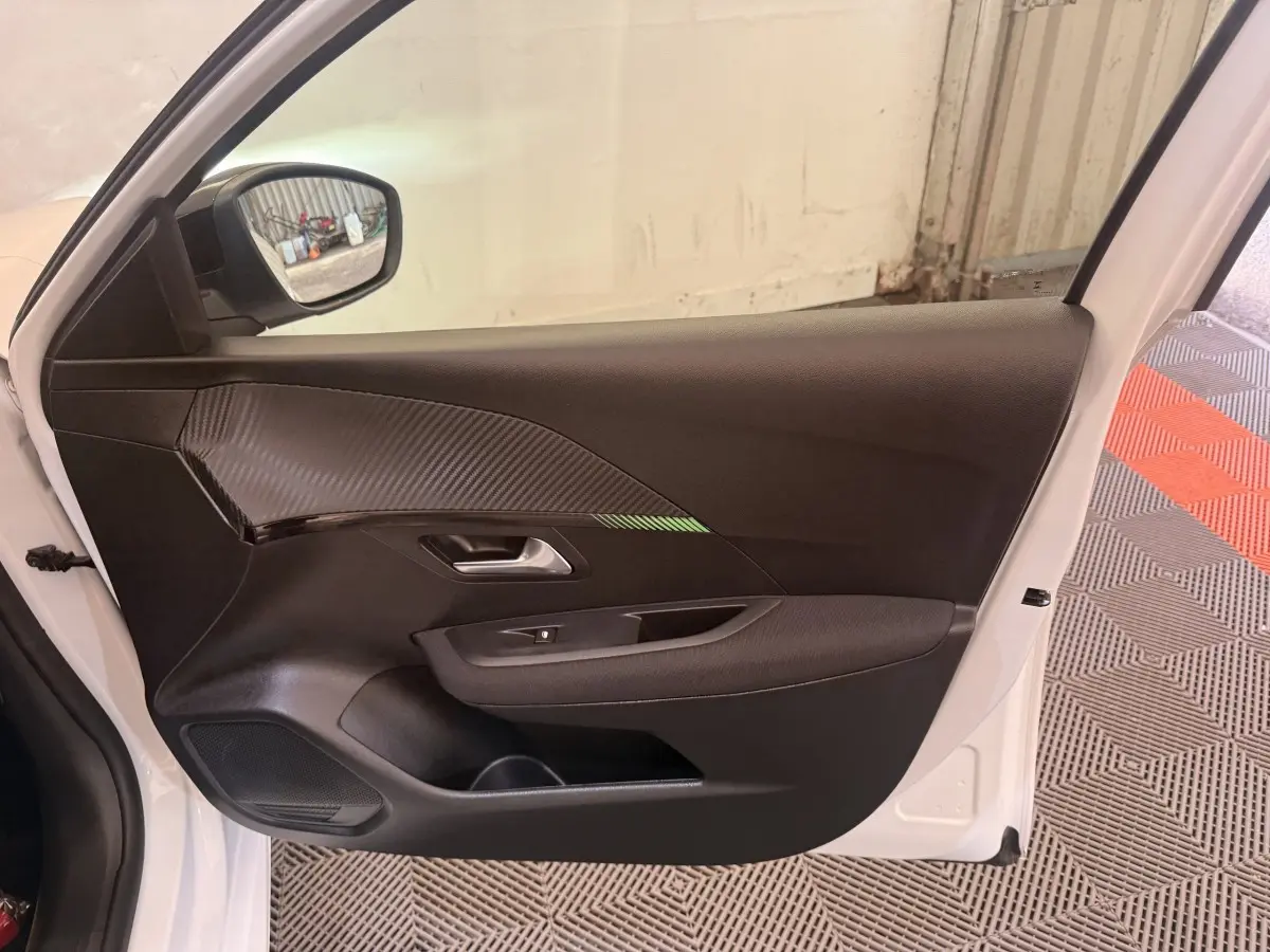 Vue côté gauche de la porte avant blanche d’une Peugeot 208 2025 avec garniture noire et insert effet carbone.