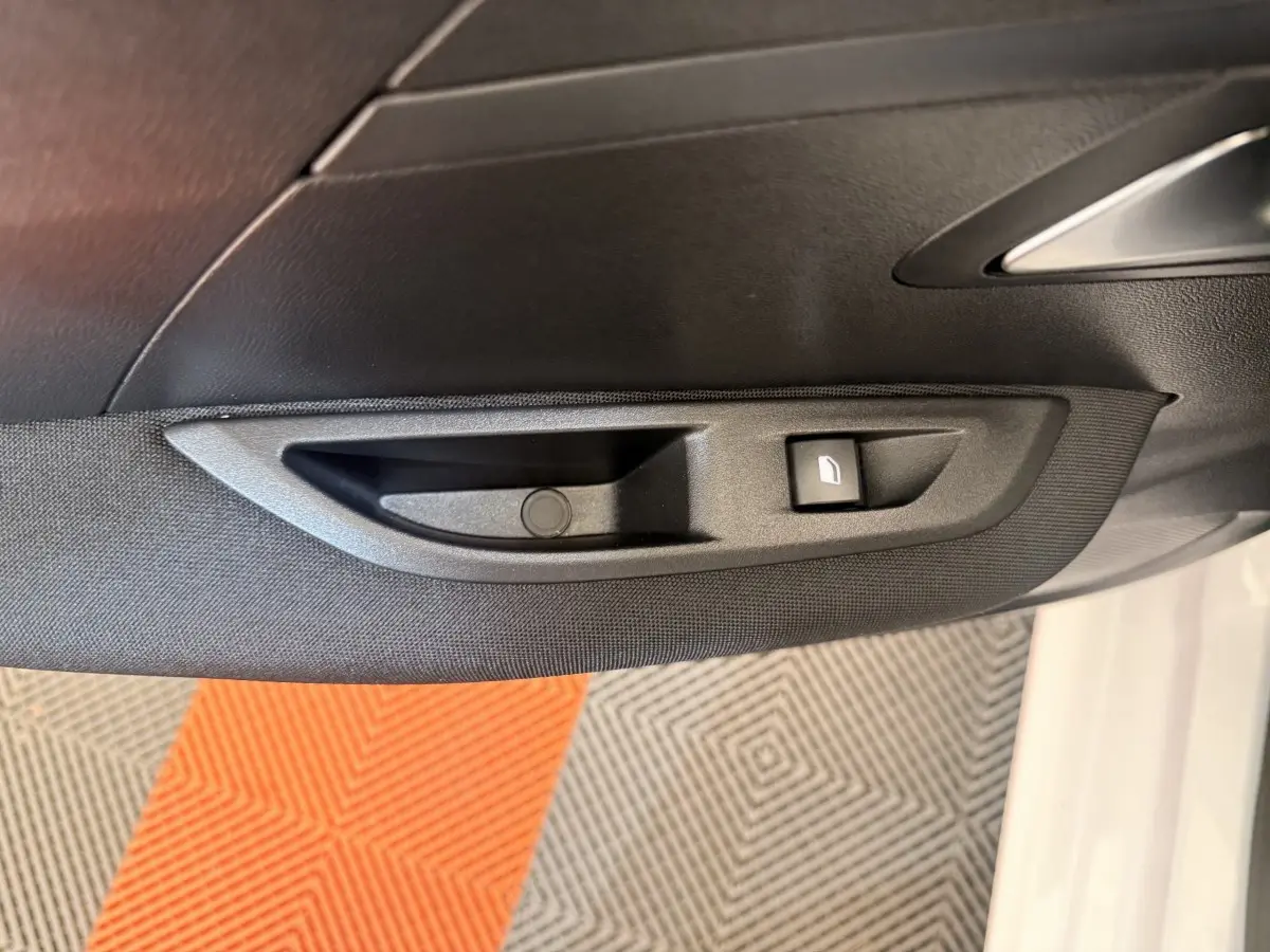 Poignée intérieure côté gauche avec bouton de lève-vitre sur porte d’une Peugeot 208 blanche vue de près.