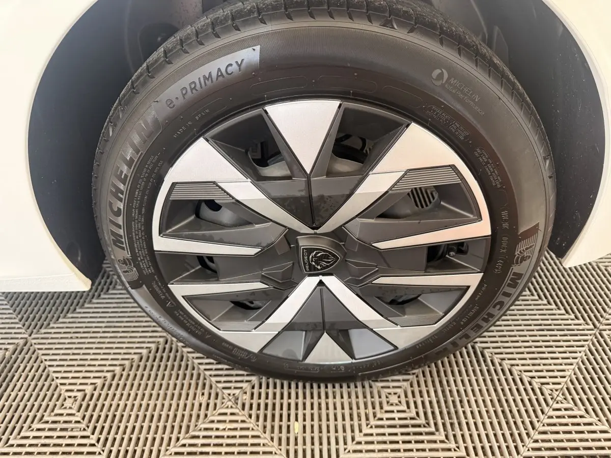 Gros plan sur la roue avant droite blanche de la Peugeot 208 avec jante en alliage noir et argent au design géométrique.
