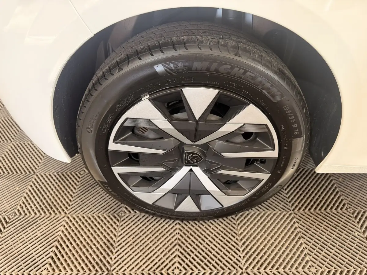 Gros plan sur la roue avant droite blanche d'une Peugeot 208 2025 avec jante au design géométrique noir et argent.