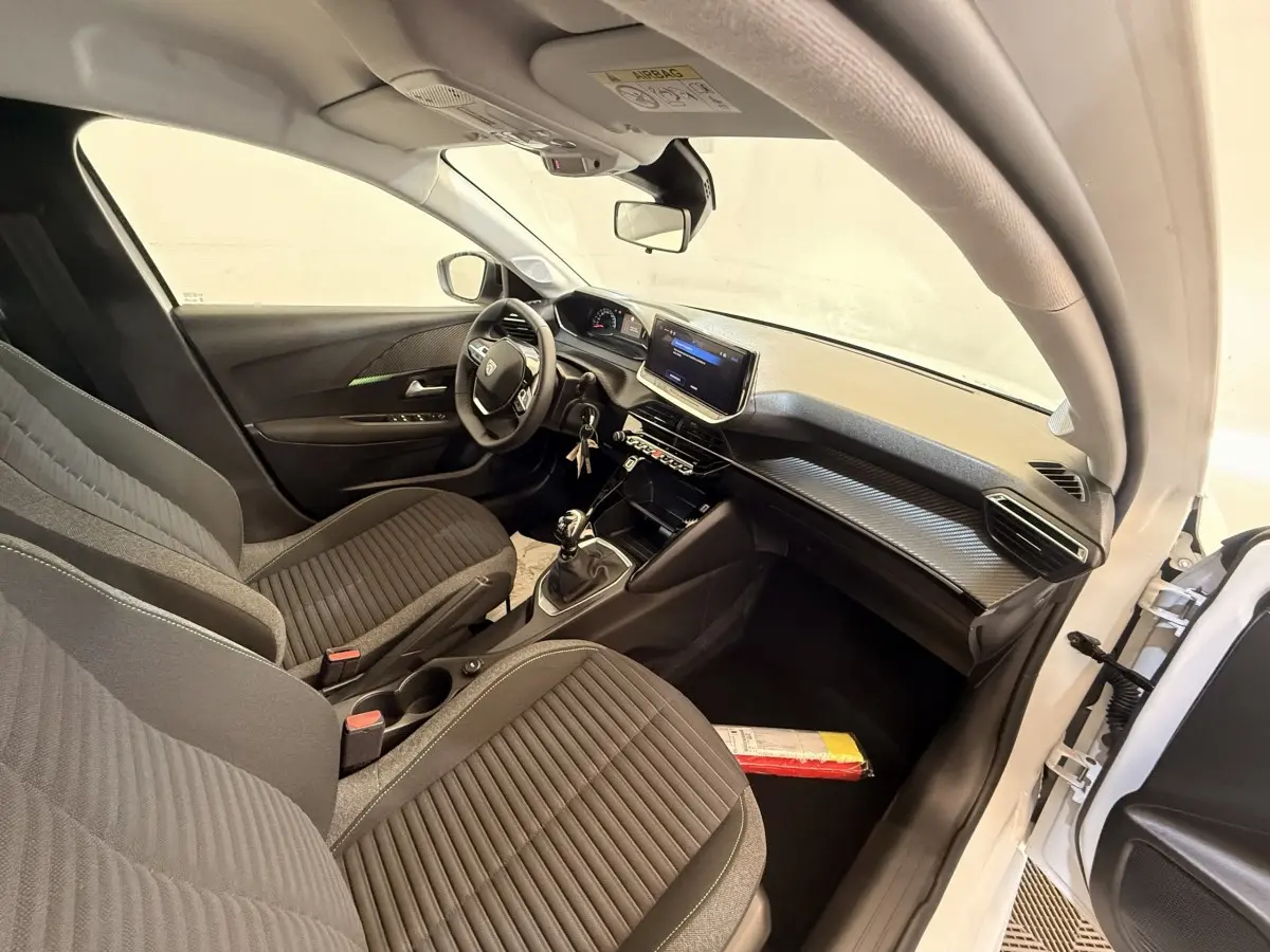 Intérieur de la Peugeot 208 blanche vue côté conducteur, montrant sièges noirs, volant cuir et écran tactile central.