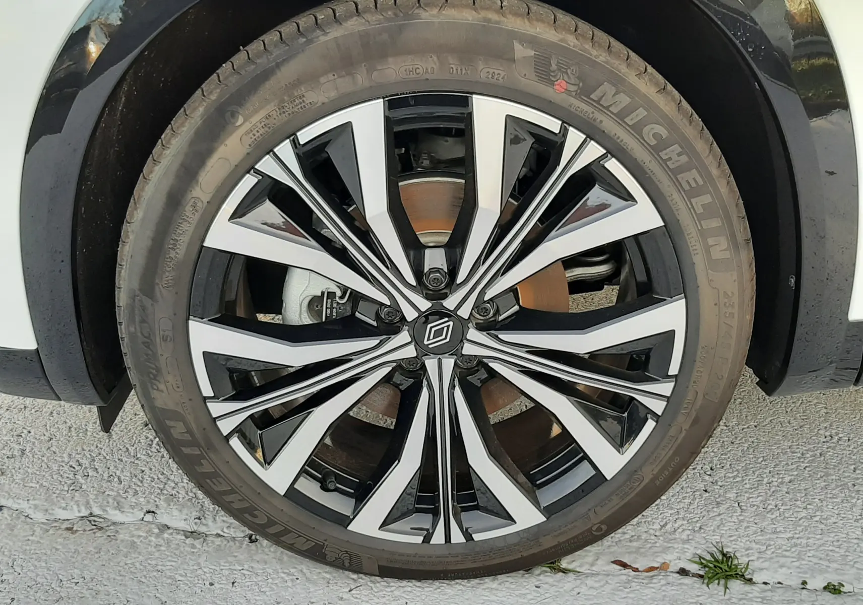Gros plan sur la roue avant droite du Renault Austral blanc nacré avec jante alliage noire et argentée design moderne.