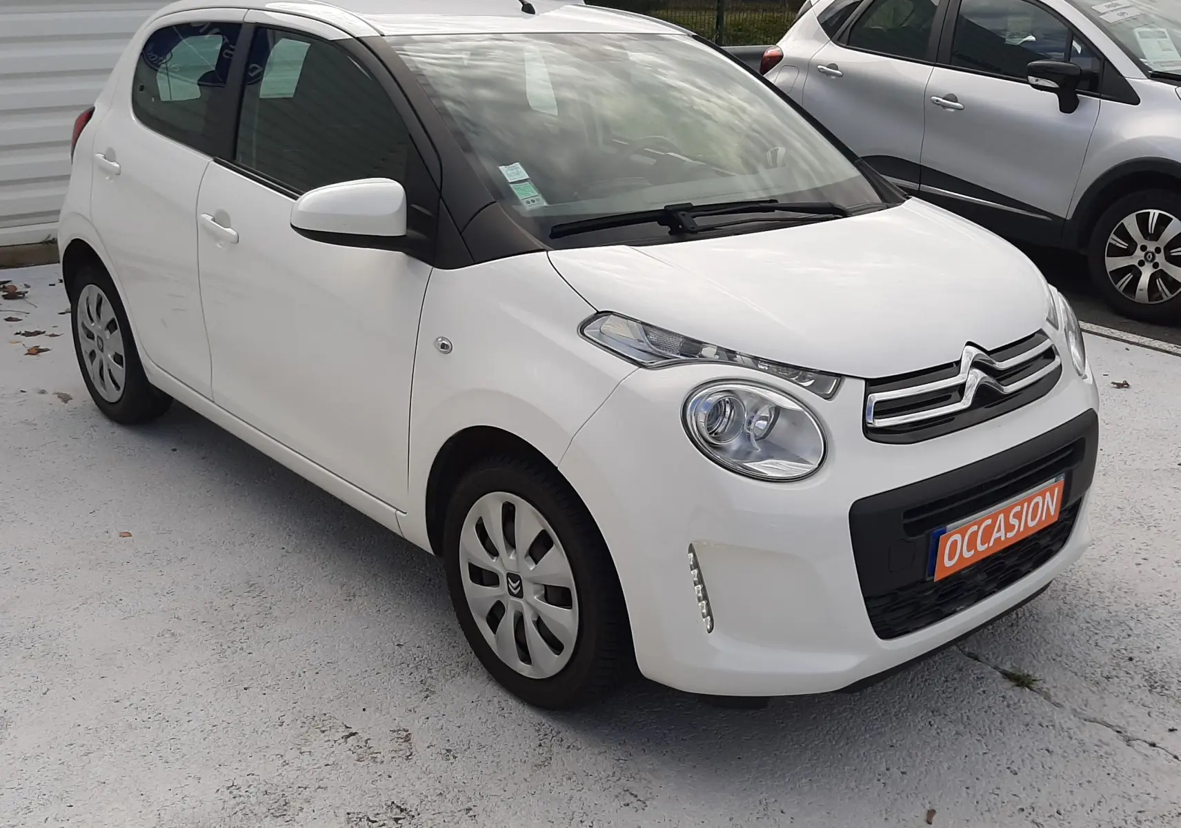 Citroën C1 blanche vue 3/4 avant droit, compacte avec calandre chromée et plaque "OCCASION" orange.