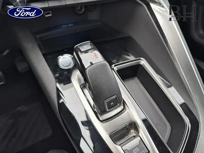 Gros plan sur la console centrale avec levier de vitesse automatique et bouton start/stop dans un intérieur noir.