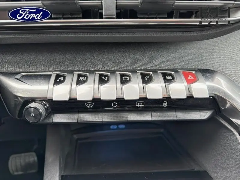 Gros plan sur la rangée de boutons chromés du tableau de bord d’un Peugeot 5008 gris Amazonite, avec touches fonctionnelles et alerte.