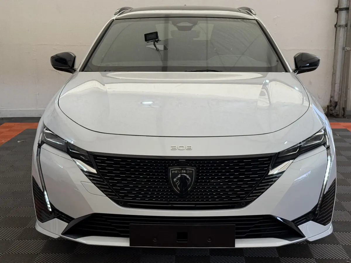 Vue frontale d'une Peugeot 308 Hybrid 136 e-DCS6 GT blanche avec calandre noire et feux LED verticaux.