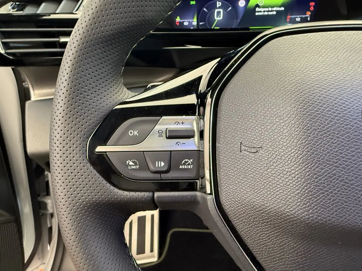 Gros plan sur le volant cuir perforé de la Peugeot 308 Hybrid 136 e-DCS6 GT avec commandes multifonctions à gauche.