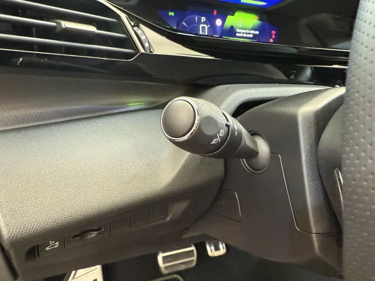 Gros plan sur la commande d’éclairage à gauche du volant dans l’habitacle noir du Peugeot 308 Hybrid 136 e-DCS6 GT 2024.