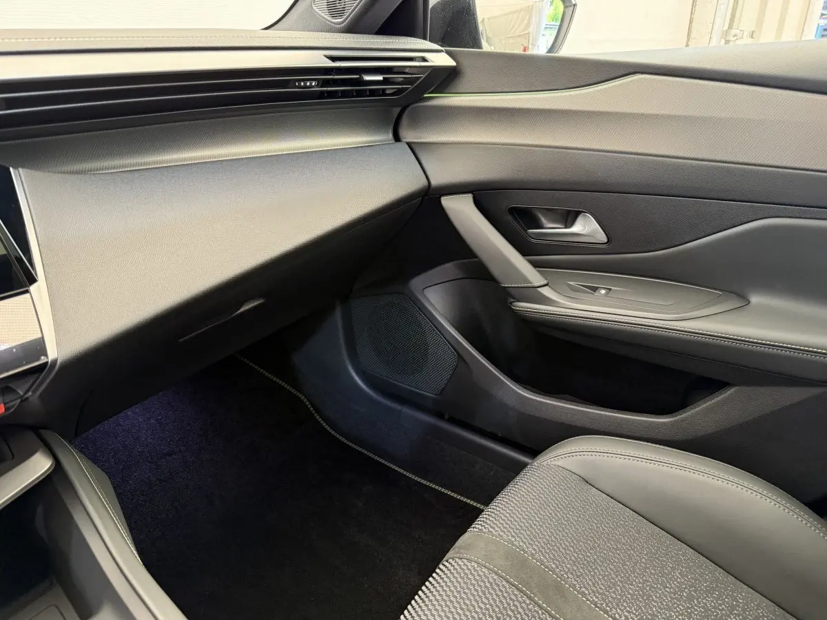 Intérieur côté passager de la Peugeot 308 Hybrid 136 e-DCS6 GT 2024, avec sellerie grise et tableau de bord noir.