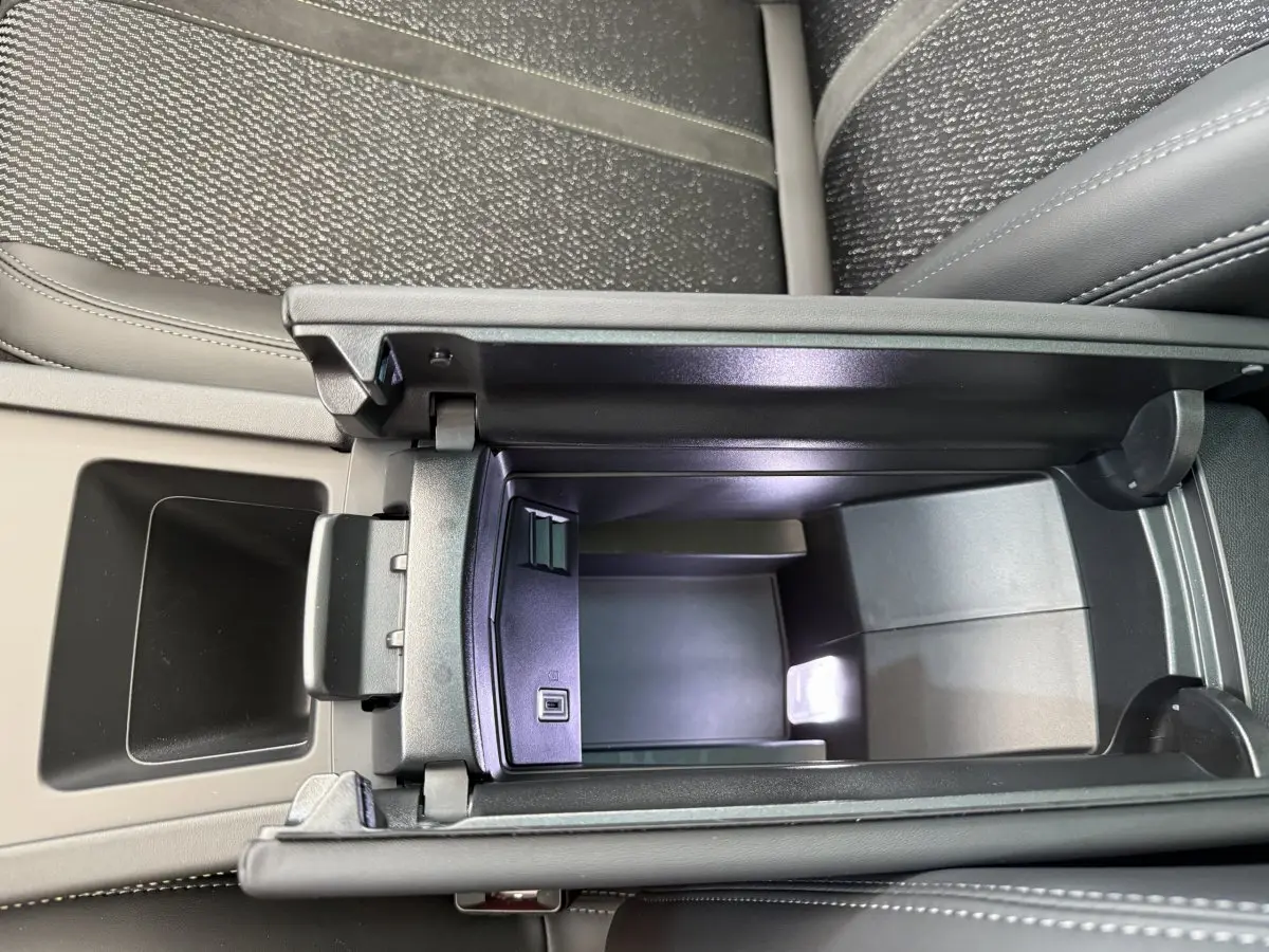 Vue rapprochée de l'accoudoir central ouvert avec compartiment de rangement et port USB dans l'habitacle du Peugeot 308 Hybrid blanc.