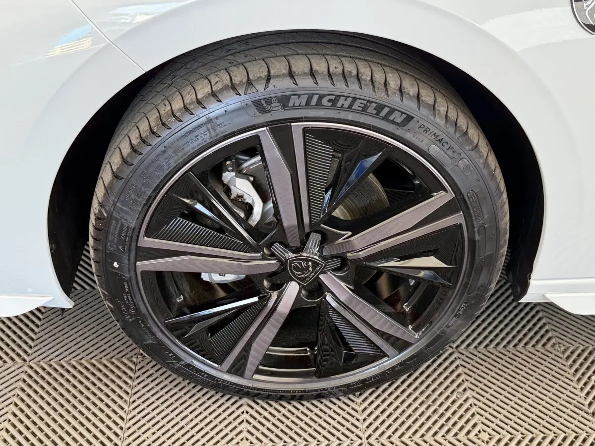 Gros plan sur la roue avant gauche de la Peugeot 308 Hybrid blanche, mettant en valeur la jante noire et argentée au design moderne.