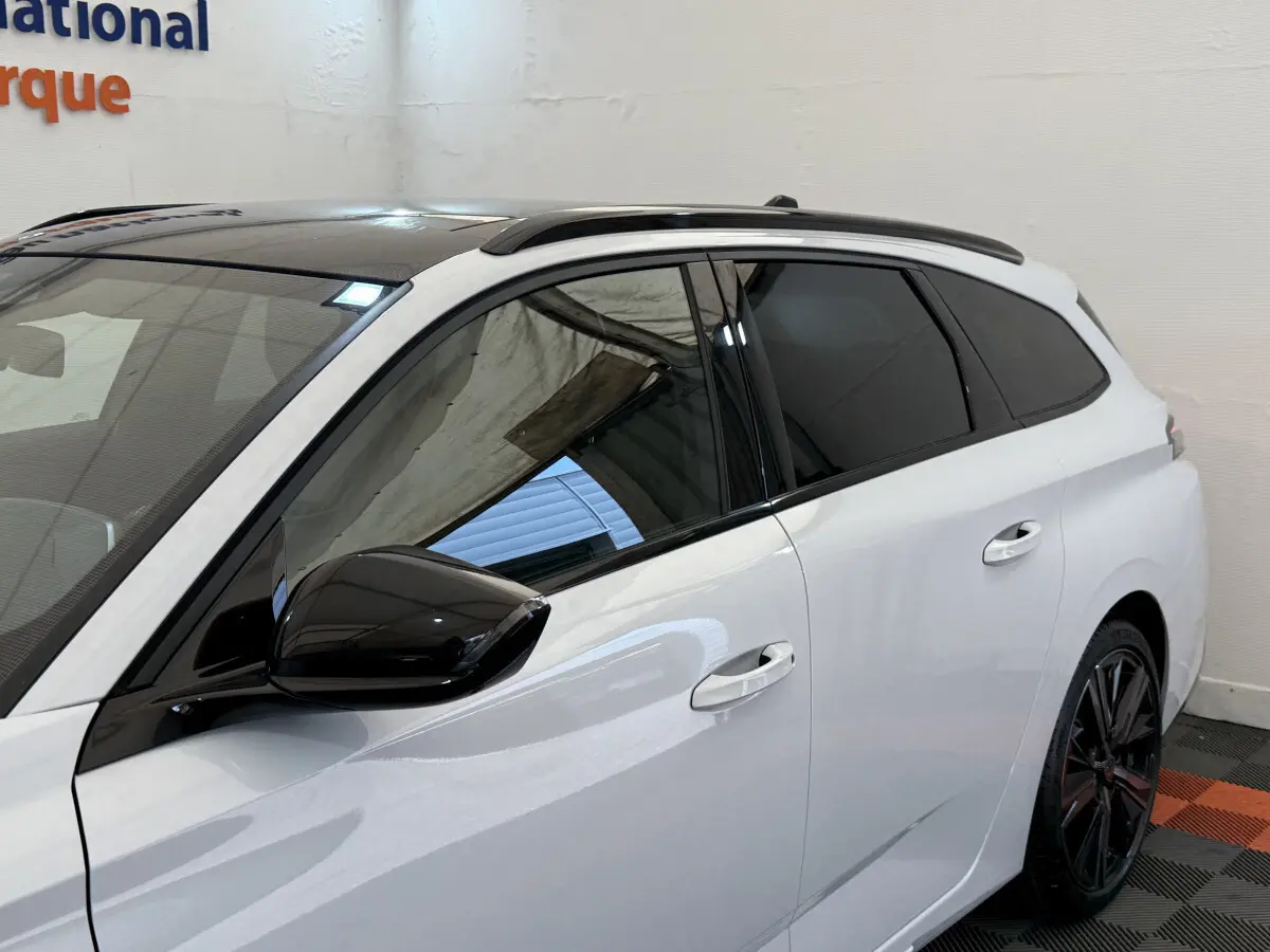 Vue latérale gauche d'une Peugeot 308 Hybrid 136 e-DCS6 GT blanche avec toit et rétroviseur noirs, jantes noires.