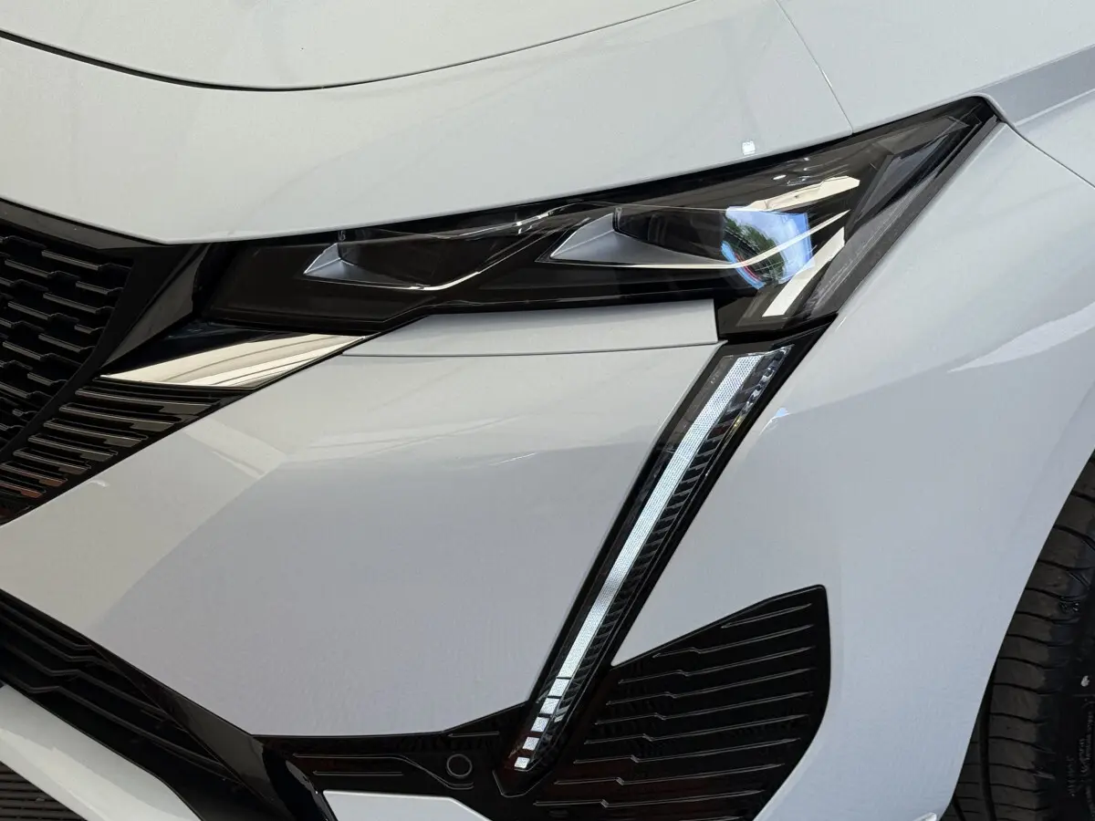 Gros plan sur le phare avant droit blanc du Peugeot 308 Hybrid 136 e-DCS6 GT avec éclairage LED distinctif en forme de griffes.