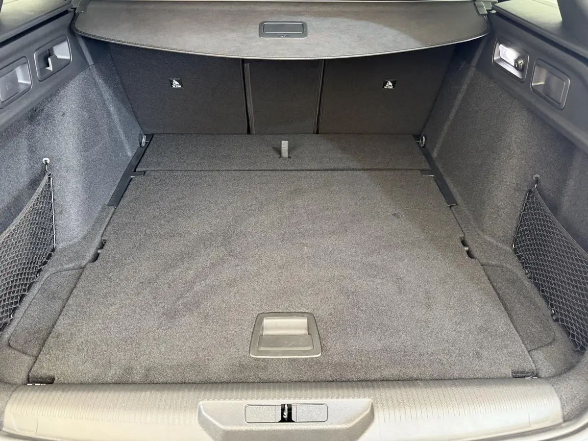 Coffre spacieux de Peugeot 308 Hybrid 136 e-DCS6 GT 2024, vue intérieure arrière avec tapis gris et filets latéraux.