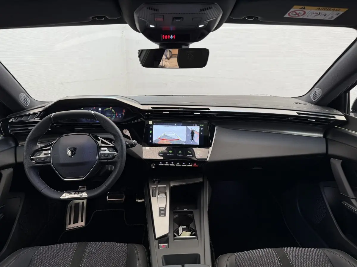Vue intérieure frontale du tableau de bord de la Peugeot 308 Hybrid 136 e-DCS6 GT 2024 avec écran tactile et volant cuir noir.