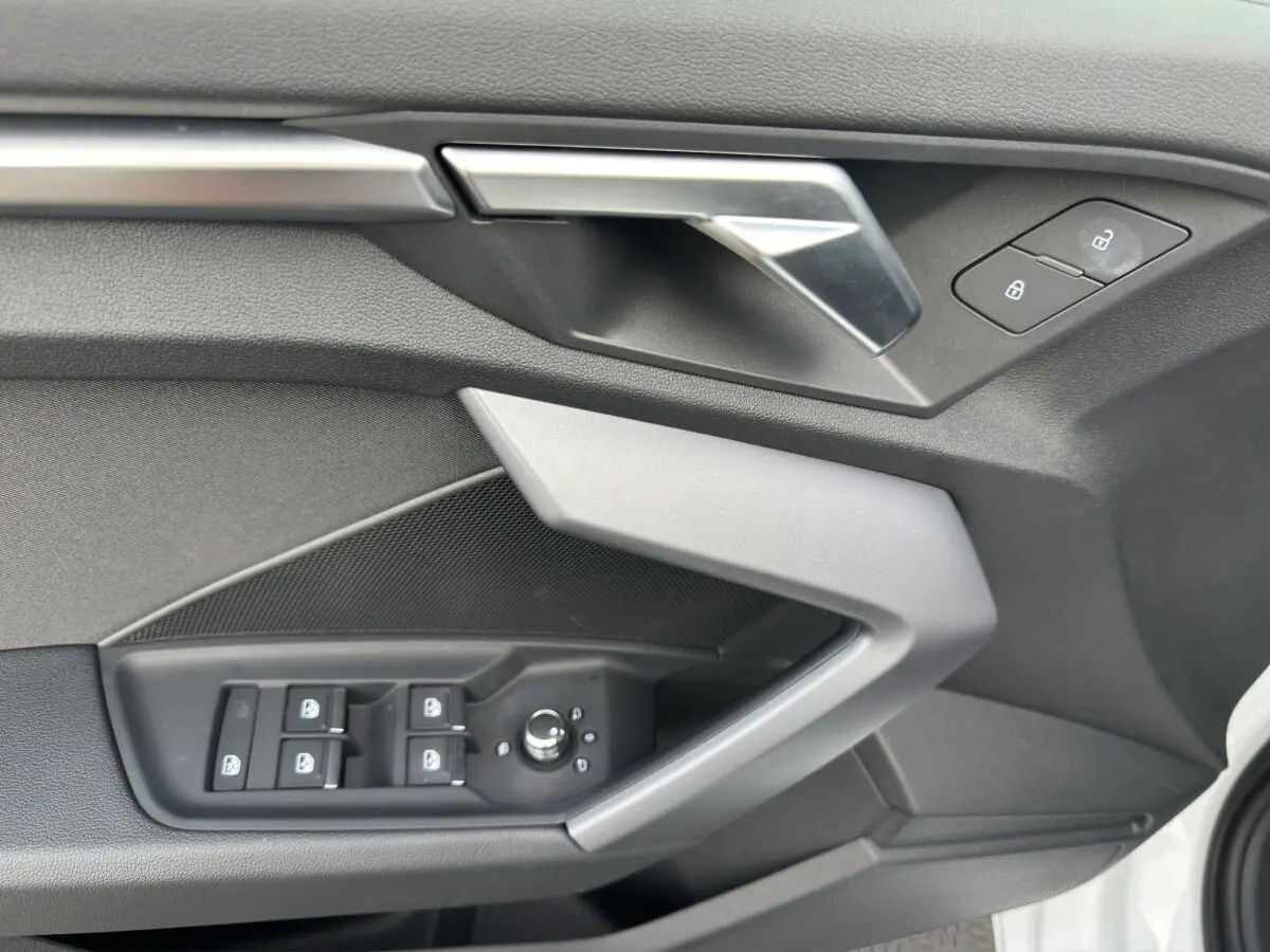 Détail de la porte avant gauche de l’Audi A3 2024 blanche, montrant les commandes de vitres et la poignée intérieure argentée.