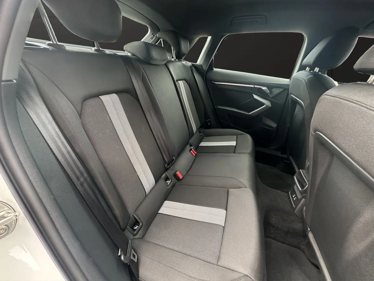 Vue intérieure arrière côté gauche de l'Audi A3 blanc 2024, montrant les sièges arrière en tissu avec bandes grises.