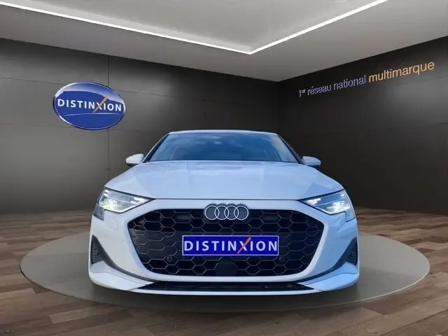 Audi A3 30 TFSI blanc vue de face, calandre hexagonale noire et phares LED allumés dans un showroom.