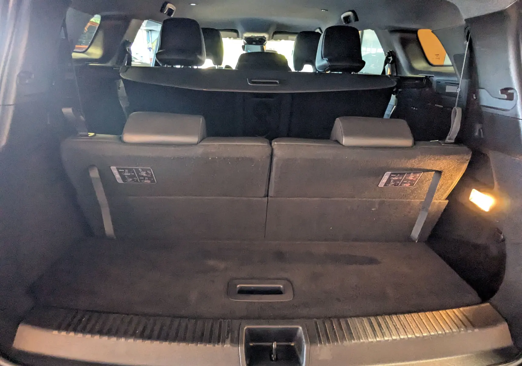 Vue intérieure arrière du coffre du Renault Espace VI noir étoile avec sièges rabattus et éclairage latéral allumé.