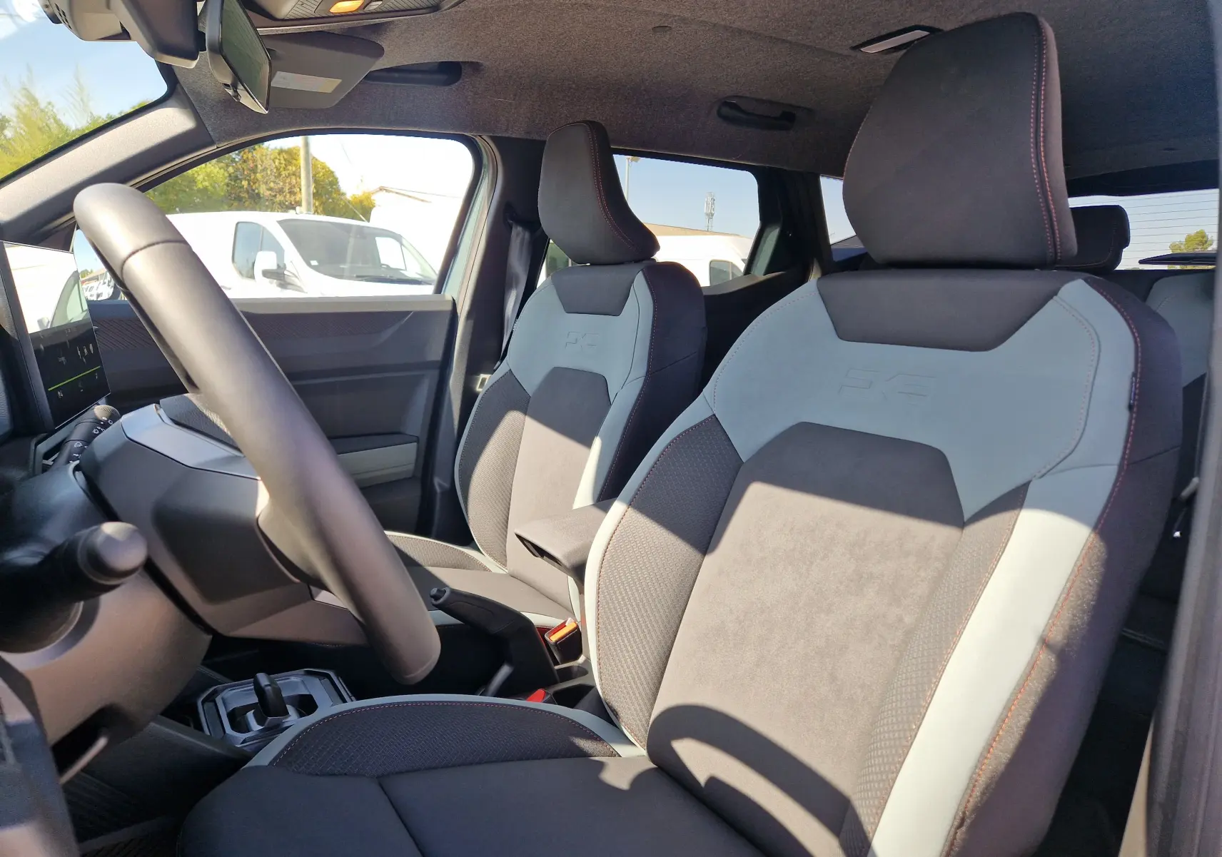 Vue intérieure côté conducteur du Dacia Duster 1.8 Hybrid 155 Extreme, sièges bi-matière gris clair et noir avec surpiqûres rouges.