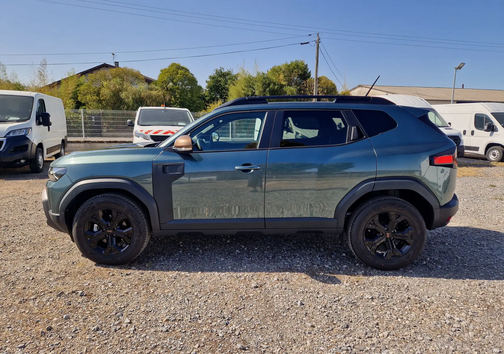 Vue de profil droit du Dacia Duster 1.8 Hybrid 155 Extreme vert cèdre avec jantes noires et coques de rétroviseur bronze.