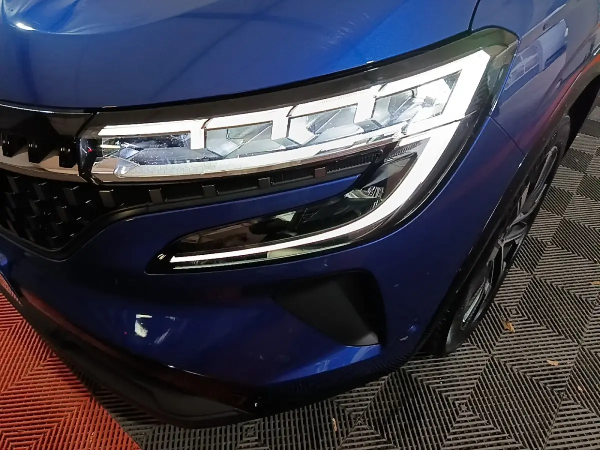 Gros plan sur l'avant droit bleu du Renault Austral 2024, mettant en valeur le phare LED et la calandre distinctive.