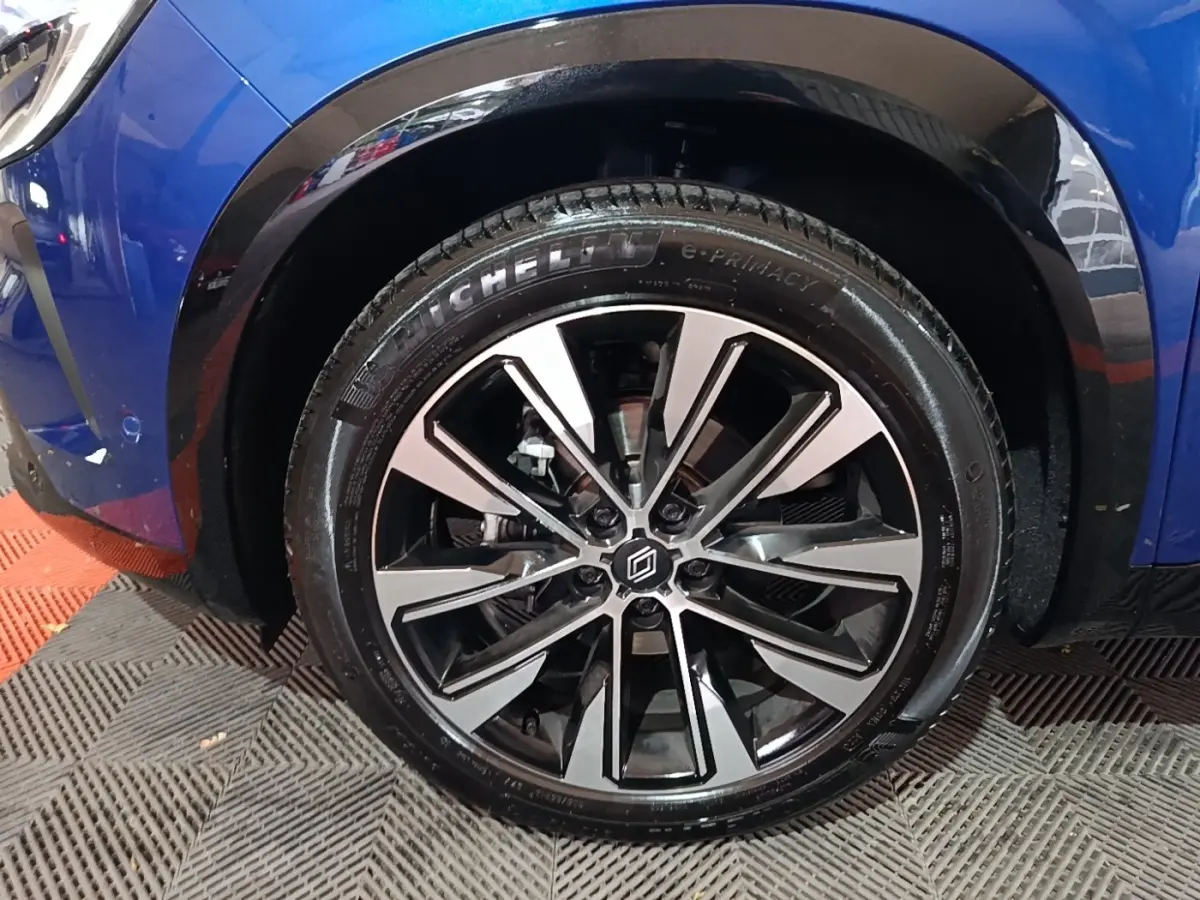 Gros plan sur la roue avant droite d’un Renault Austral bleu, jante alliage noire et argentée au design moderne.
