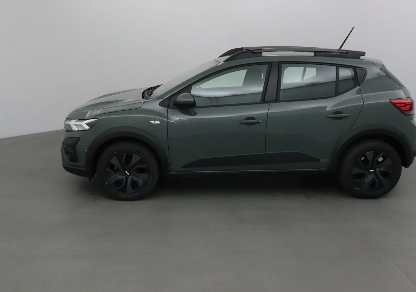 Profil côté gauche d'une Dacia Sandero Stepway 2025 en kaki Kichen avec barres de toit et jantes noires.