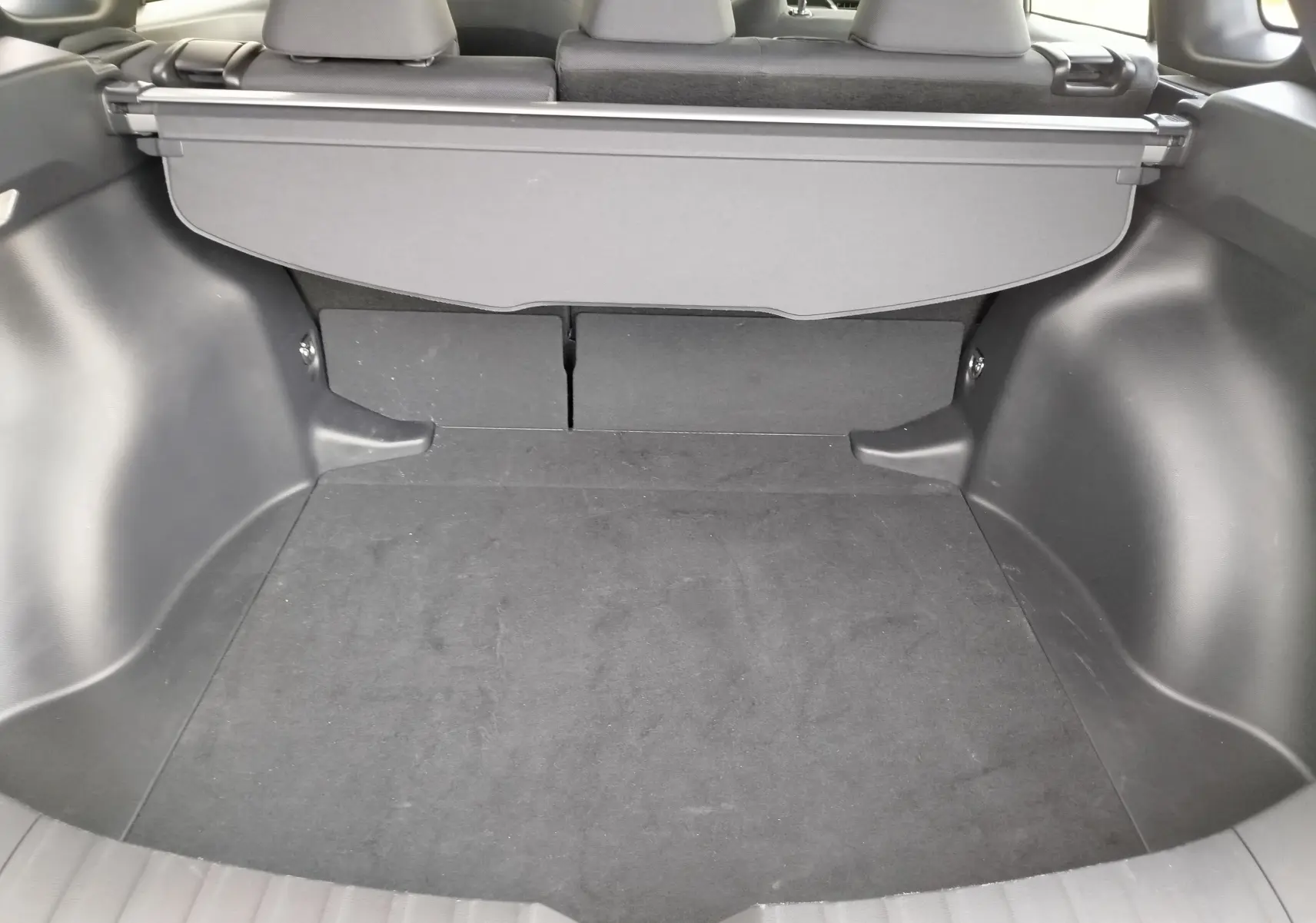 Coffre spacieux du Toyota Corolla Cross gris acier 2025, vue intérieure arrière avec cache-bagages déployé.