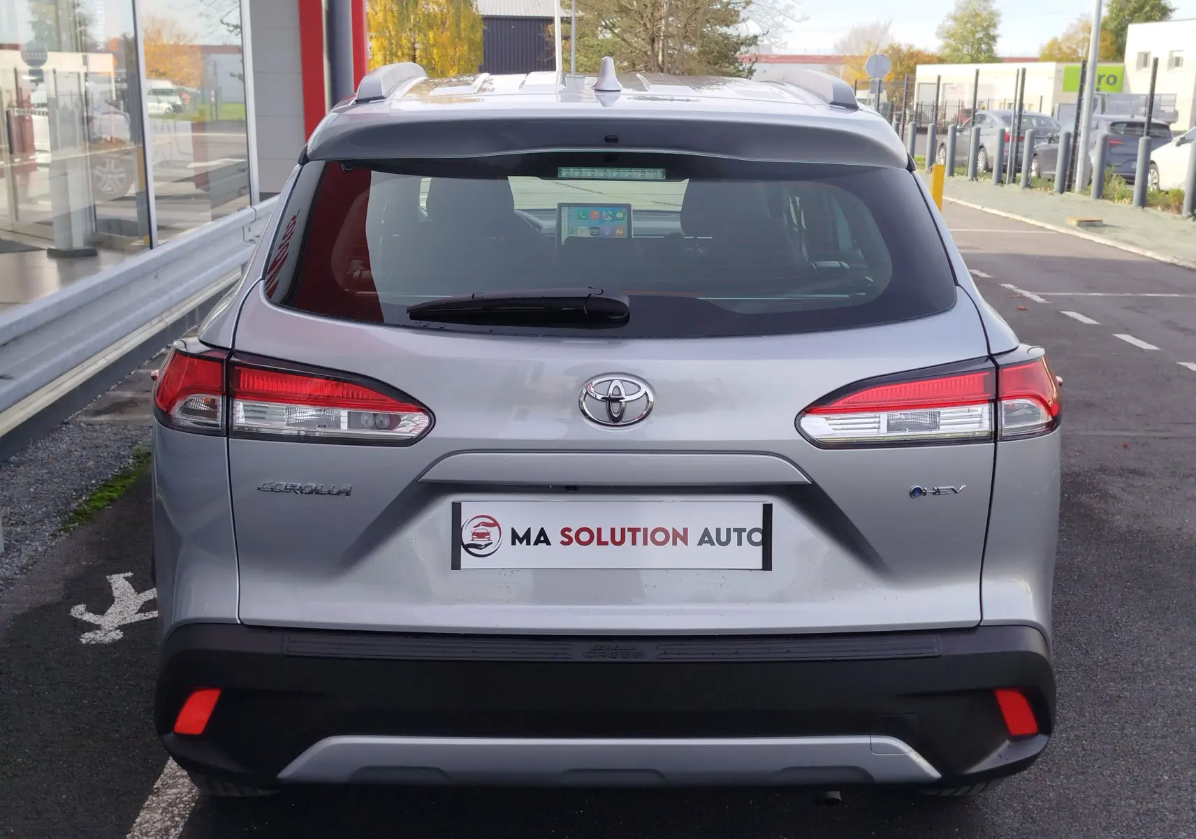 Vue arrière d'un Toyota Corolla Cross gris acier 2025 avec feux arrière allongés et logo hybride visible.