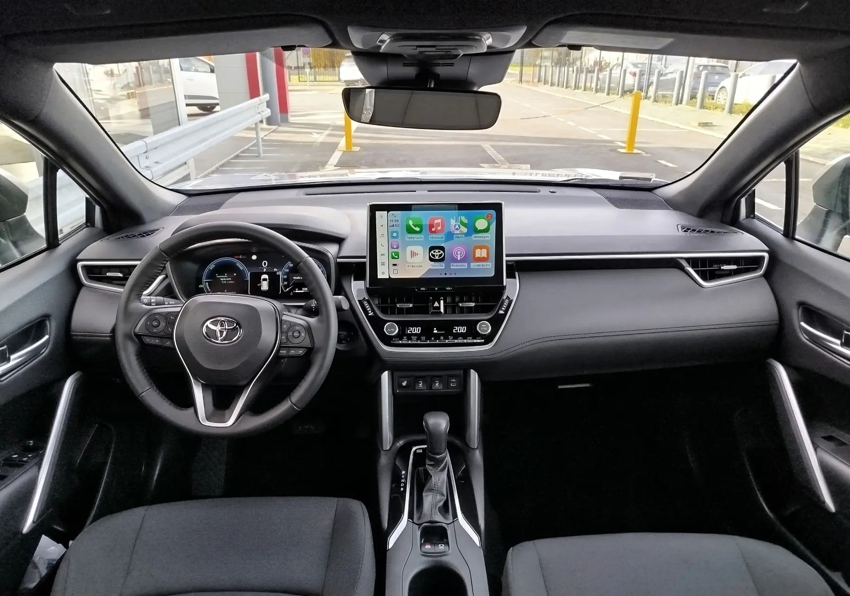 Vue intérieure avant du Toyota Corolla Cross gris acier 2025, tableau de bord moderne avec écran tactile central et volant multifonction.