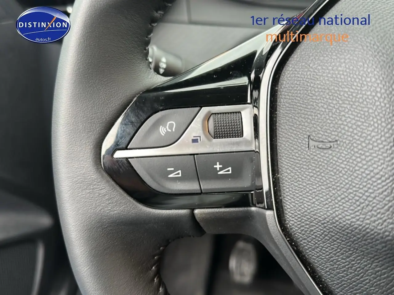 Gros plan sur les commandes audio au volant noir d'une Peugeot 208 1.2 PureTech 100 Active 2024, intérieur gris.