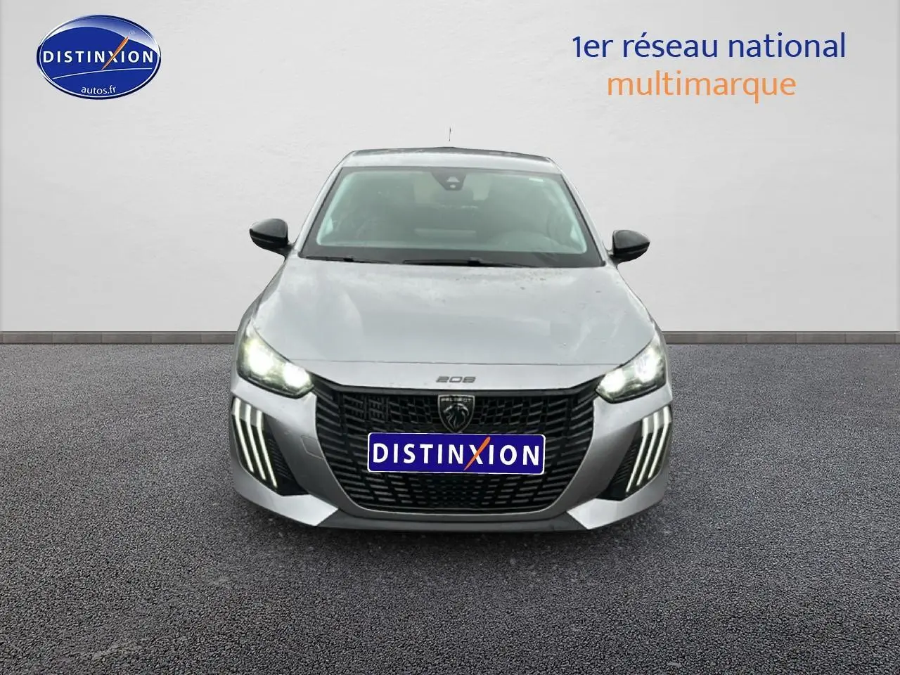 Vue frontale d'une Peugeot 208 1.2 PureTech 100 Active gris Artense avec feux diurnes LED allumés.