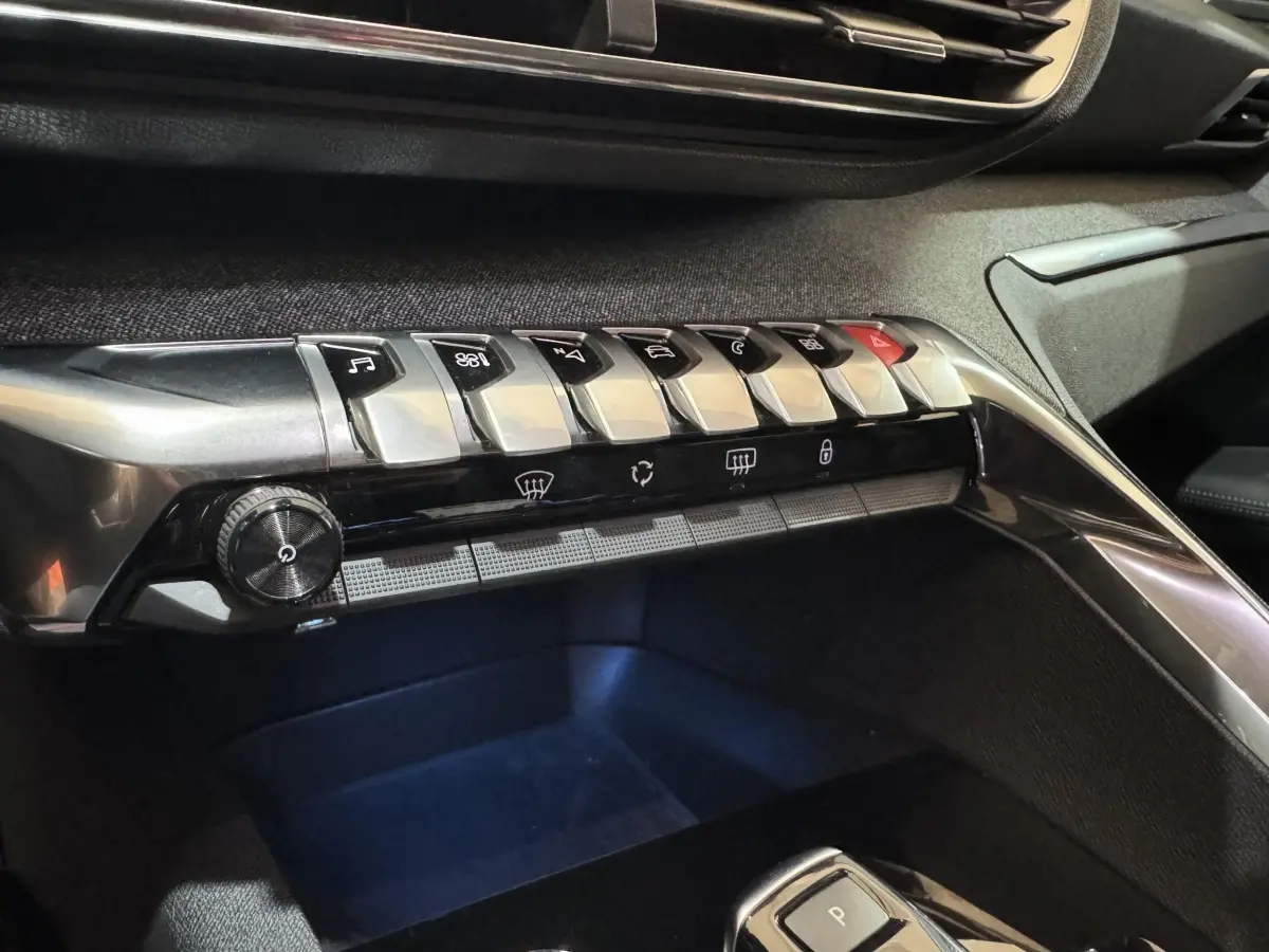 Gros plan sur la console centrale noire du Peugeot 3008 PureTech 130, mettant en valeur les boutons métalliques et commandes.