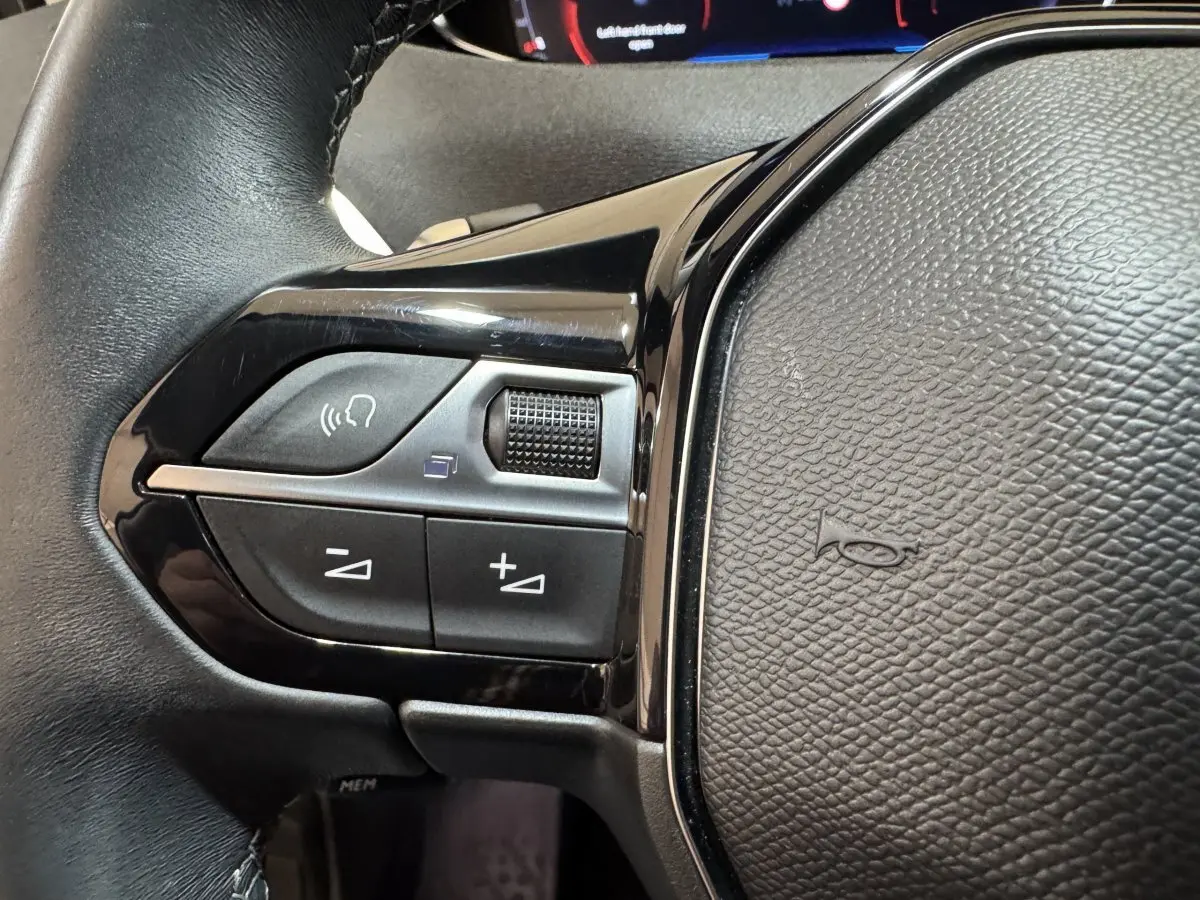 Gros plan sur les commandes gauche du volant cuir noir du Peugeot 3008 orange, avec boutons de volume et reconnaissance vocale.