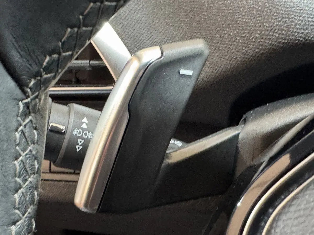 Gros plan sur la palette de changement de vitesse en aluminium et plastique noir, côté gauche du volant cuir du Peugeot 3008 orange.