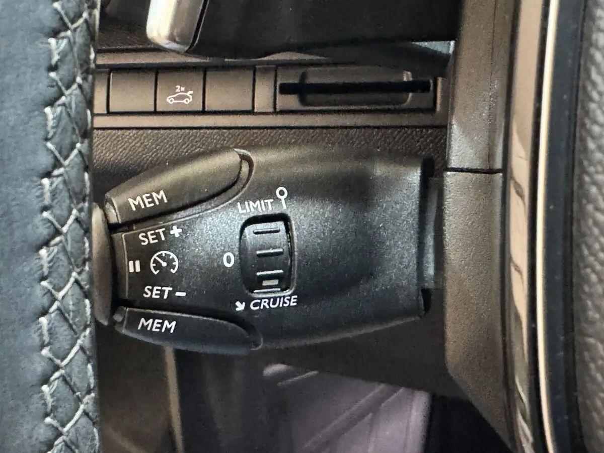 Gros plan sur la commande de régulateur de vitesse noire dans l’habitacle du Peugeot 3008 PureTech 130 orange.