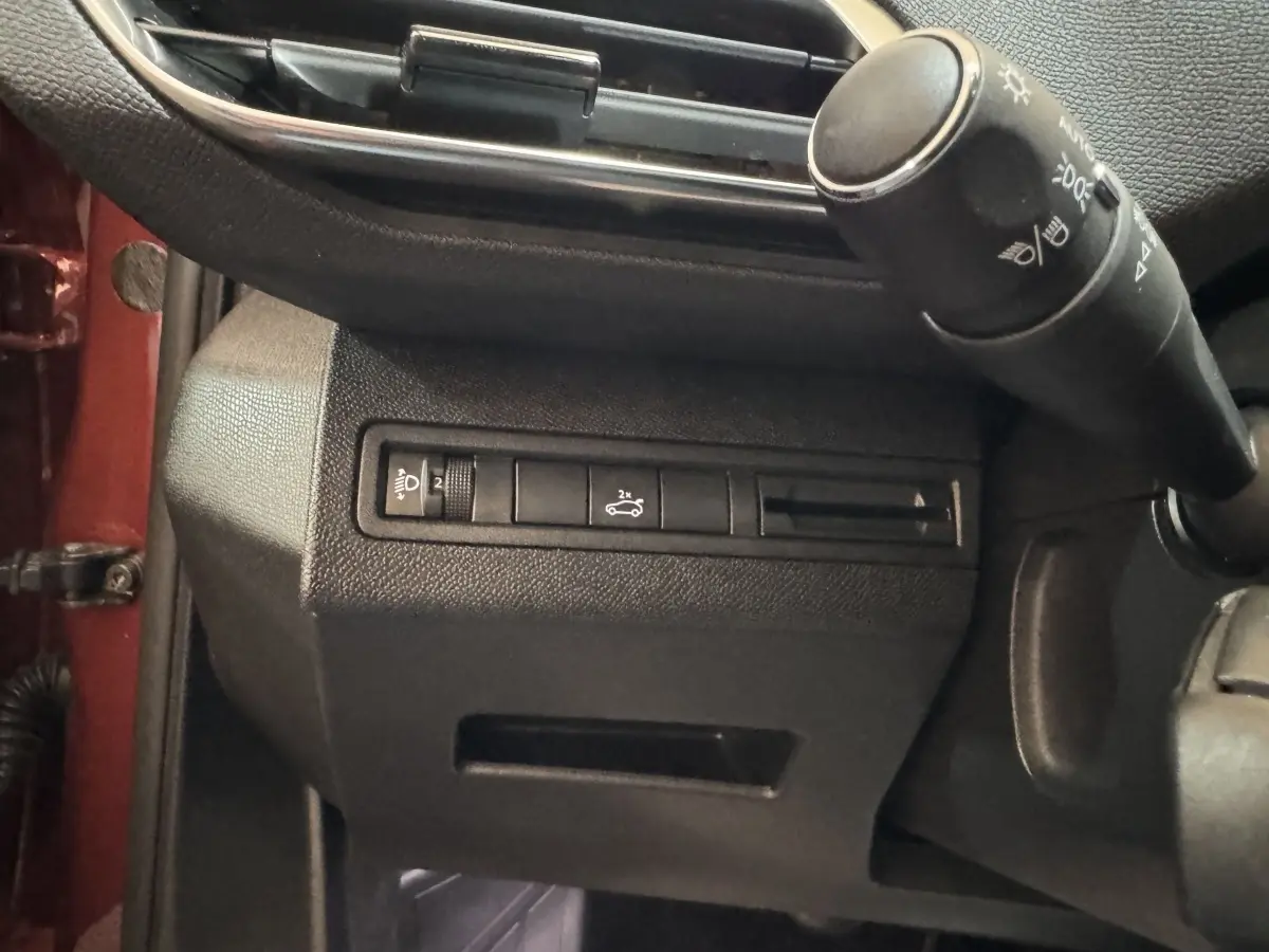 Détail intérieur côté gauche du tableau de bord noir avec commandes d’éclairage et ouverture du coffre, bord orange visible.