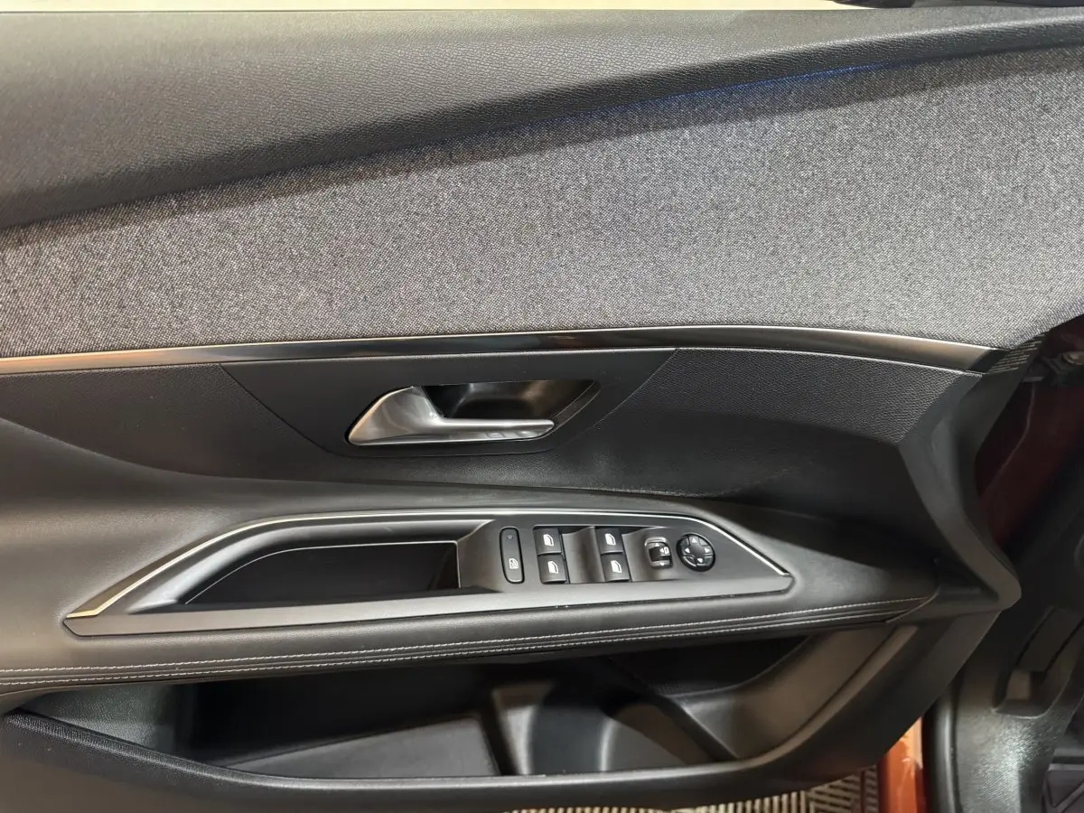 Intérieur côté gauche de la porte avant d’un Peugeot 3008 orange 2020, avec commandes des vitres et poignée argentée.