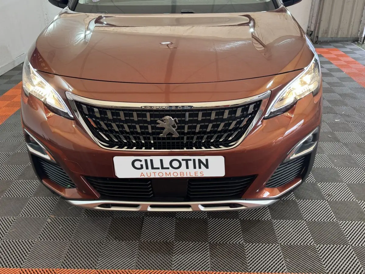 Vue avant rapprochée du Peugeot 3008 orange 2020 avec calandre chromée et phares LED allumés.