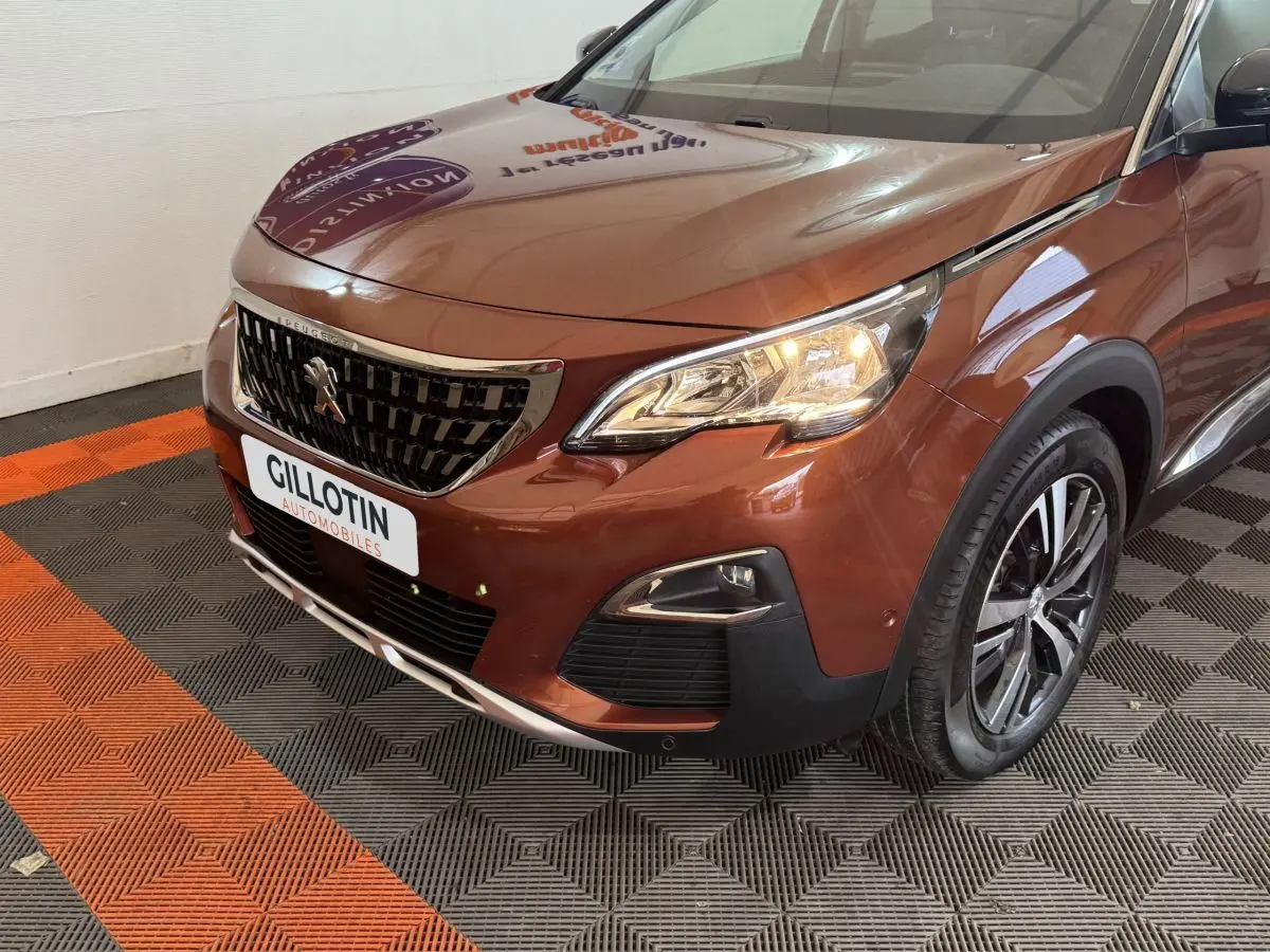 Vue 3/4 avant droit d'un Peugeot 3008 orange avec calandre noire et jantes alliage, phare allumé en intérieur showroom.