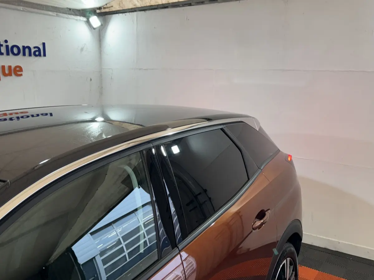 Vue 3/4 arrière droite du Peugeot 3008 orange avec toit noir et vitres teintées dans un garage.