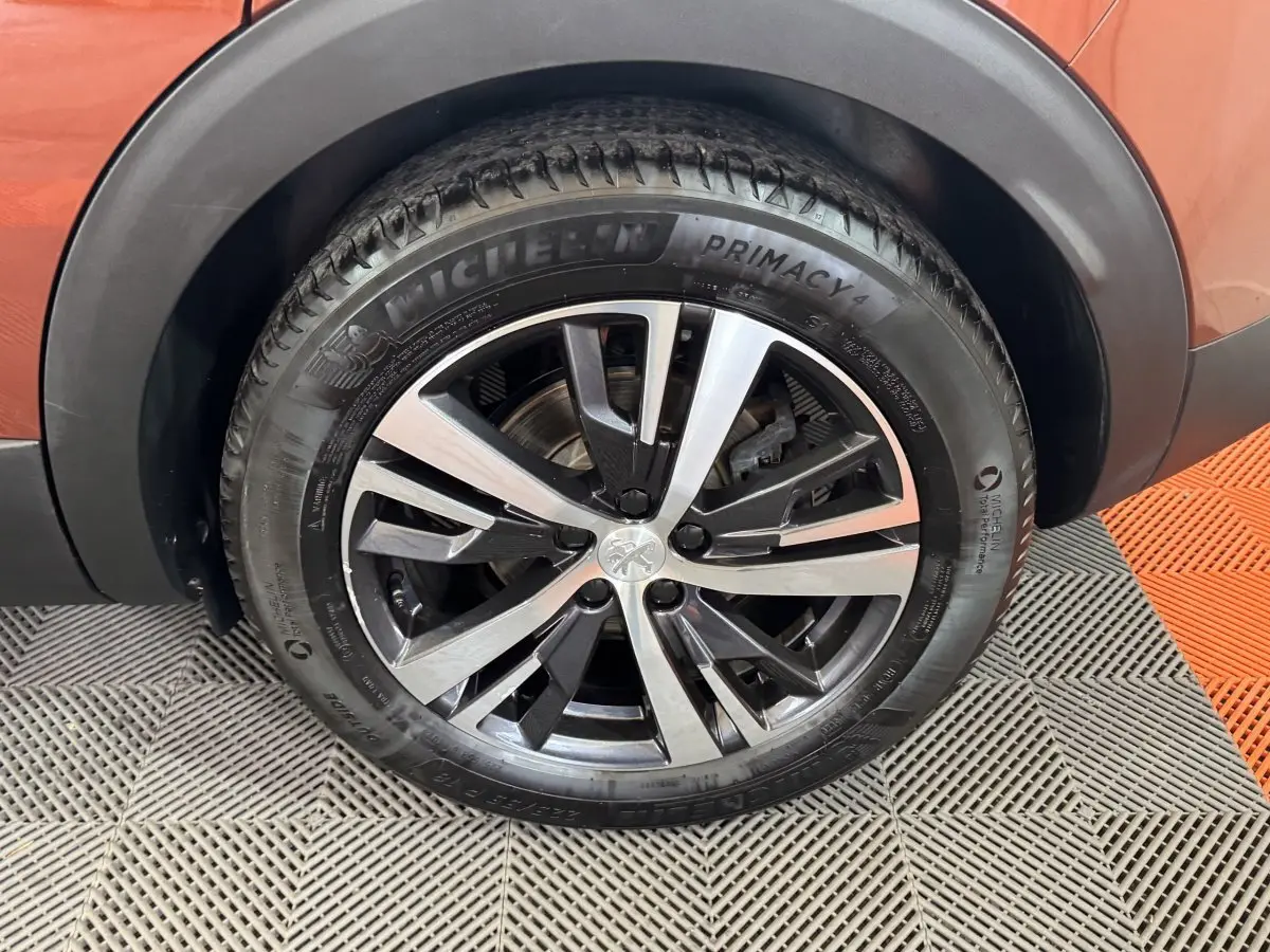 Gros plan sur la roue avant gauche orange d’un Peugeot 3008 avec jante alliage bicolore et pneu Michelin Primacy 4.